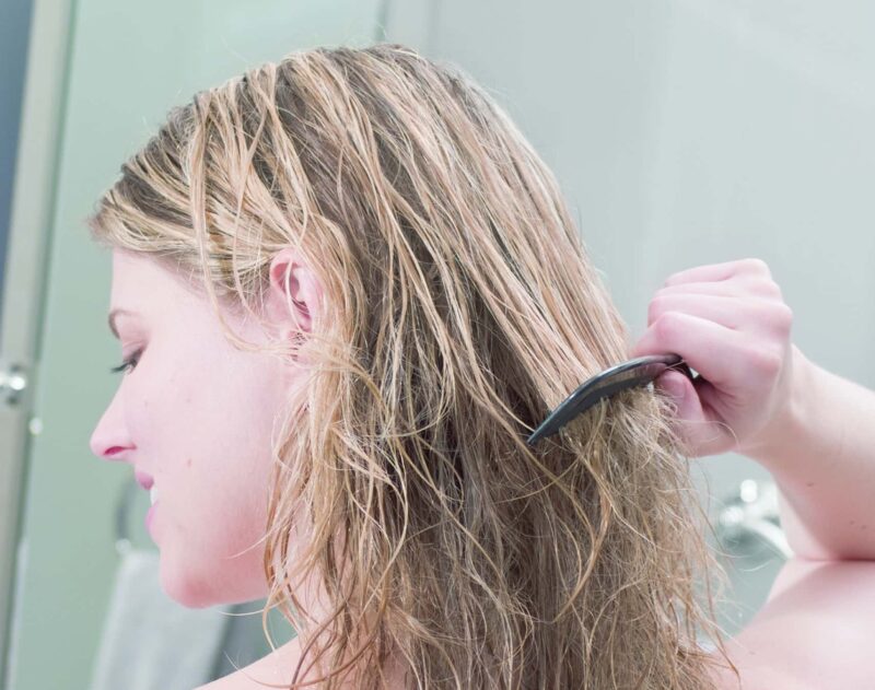 woman wrapped in a towel trying to comb her hair after a shower but can't because of hard water buildup