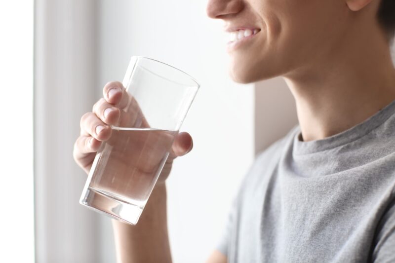 closeup of a man smiling while he holds a cup of water on his way to his mouth to drink