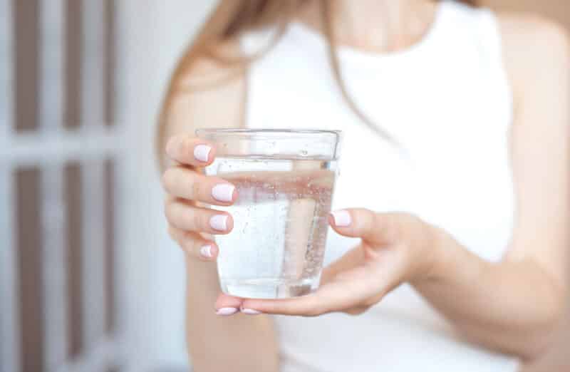 Female hands holding a clear glass of water. A glass of clean mineral water in hands, healthy drink