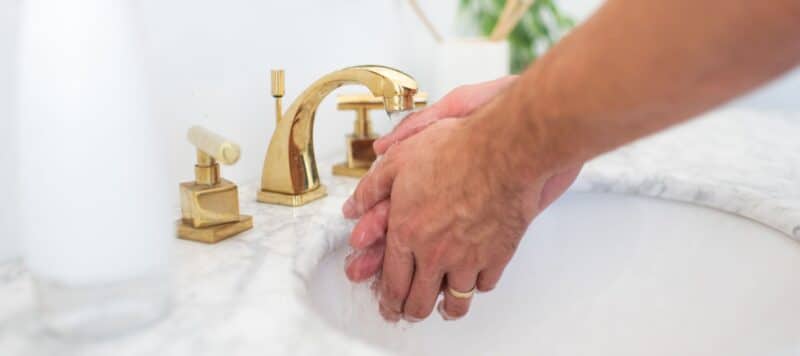 hands reaching down to a sink with gold fixtures washing hands