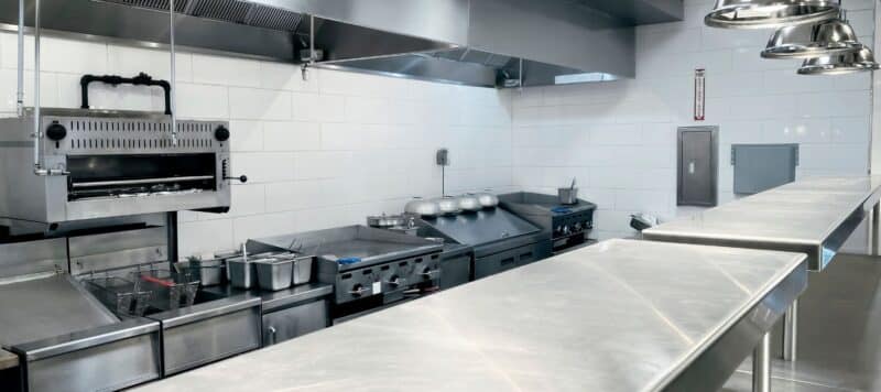 Modern commercial kitchen with stainless steel appliances, counters, and ventilation hoods